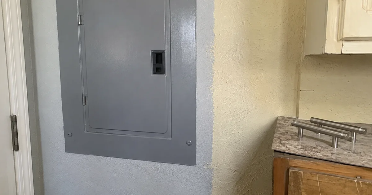 A freshly painted electrical panel cover on a kitchen wall next to visibly older, unpainted wall texture, with new cabinet hardware on an older cabinet door nearby