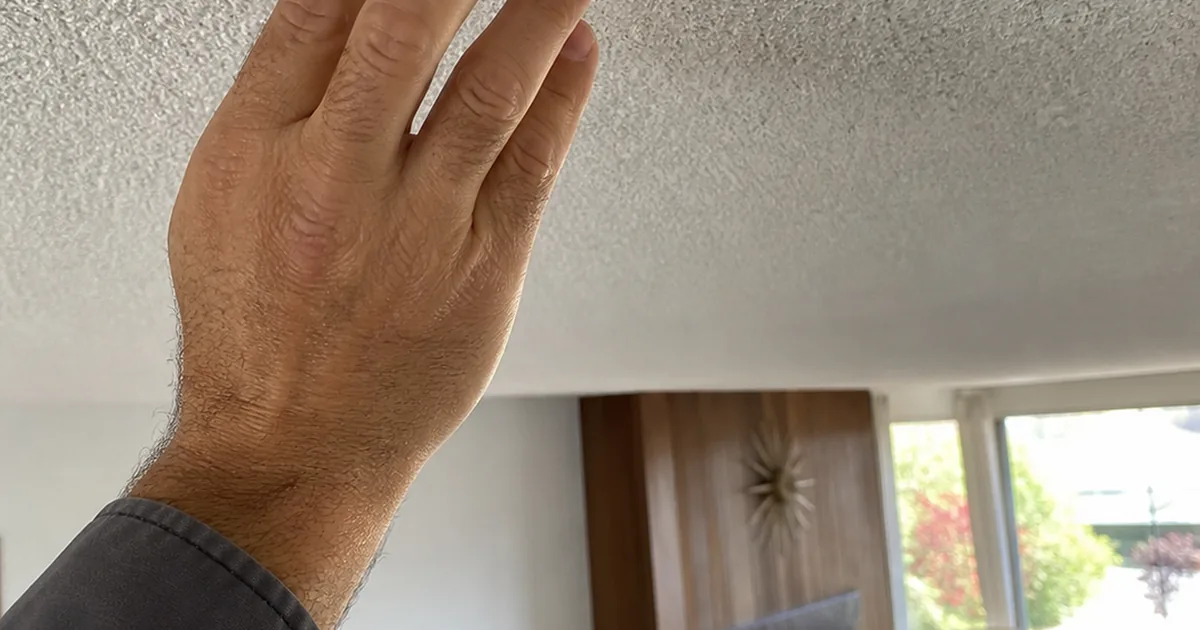 Home inspector's hand touching a textured popcorn ceiling in a sunlit mid-century Anaheim living room