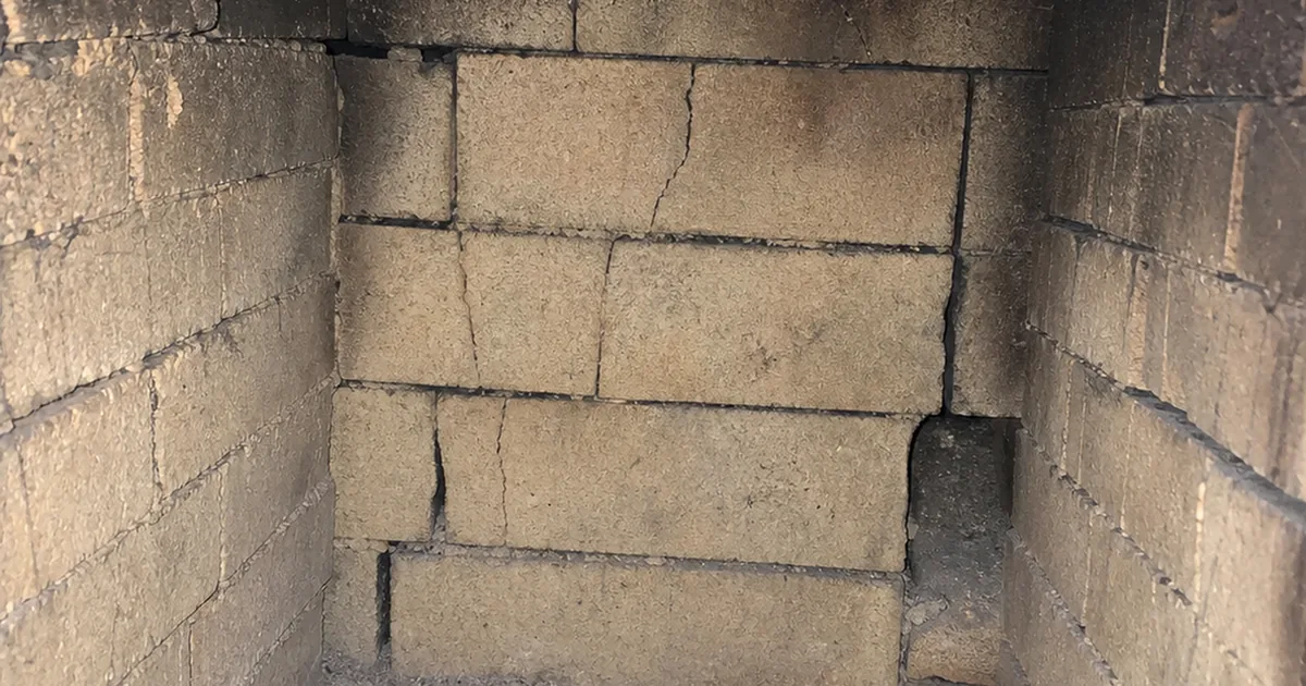 Interior of an older Brentwood masonry firebox with cracked firebrick and failed mortar joints at the back wall