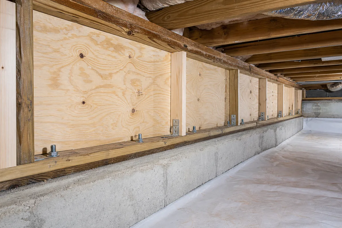 A crawlspace cripple wall newly braced with fresh plywood sheathing and shiny galvanized anchor bolts tying the framing to the concrete foundation, a completed earthquake retrofit