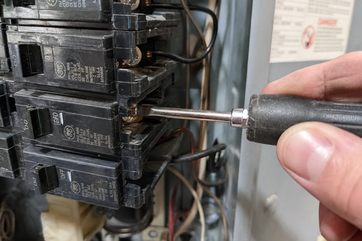 A hand using a torque driver to test the tightness of a screw terminal on a suspected double-tapped breaker lug
