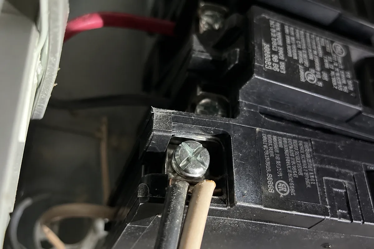 Looking upward into an open breaker panel showing a row of breakers with two wires visibly crammed under a single terminal