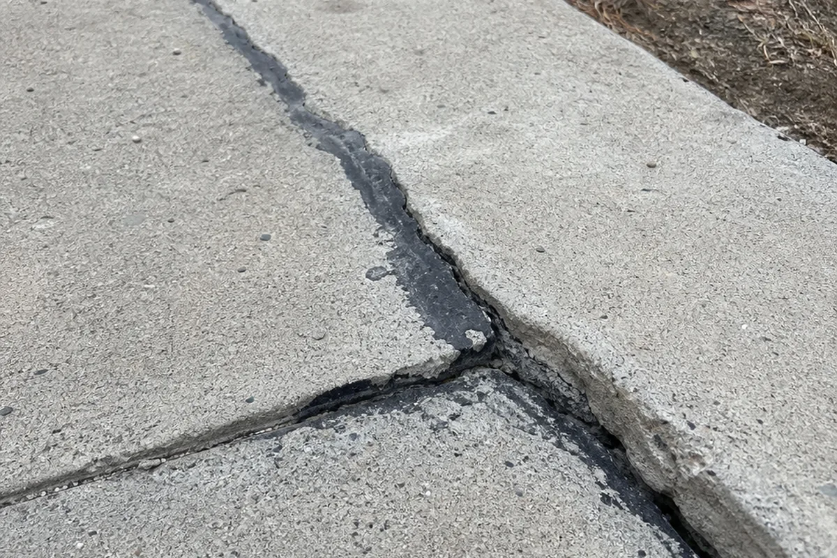 Diagonal crack across a concrete driveway that has been patched once and reopened, with old sealant pulling apart
