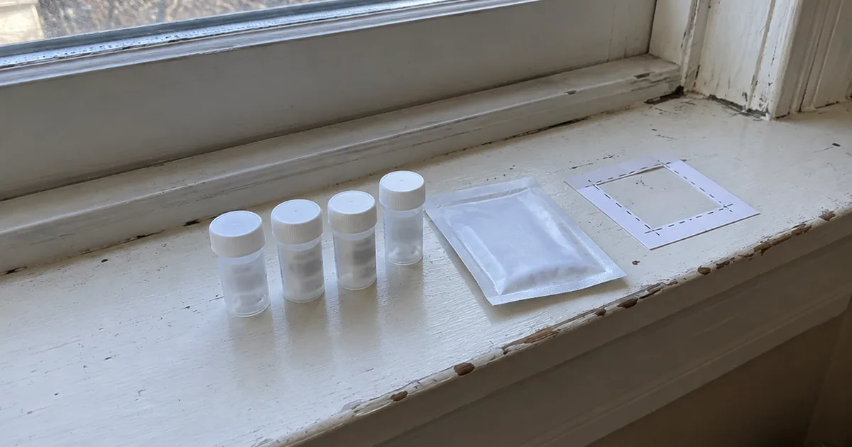 A dust-wipe sample collection kit with sample vials, a wipe packet, and a template square laid out on an older painted windowsill