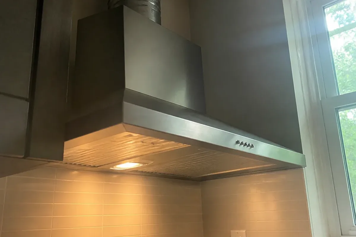 A range hood vent duct and damper above a newly installed kitchen cooktop, viewed from below in daylight