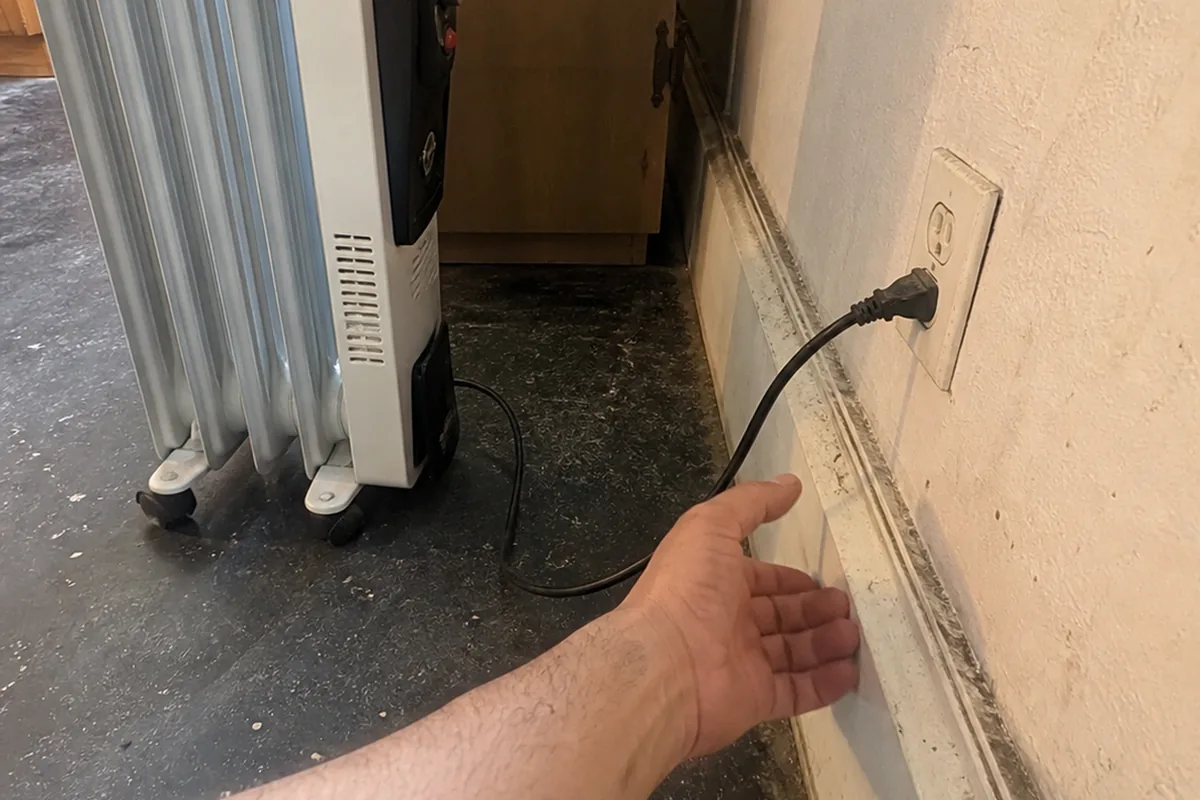 A hand checking the cord and outlet connection of a portable space heater standing in for permanent heat in a converted Fremont bedroom