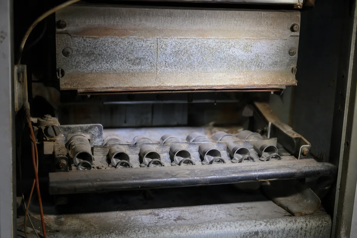 Close view into the open burner compartment of an old furnace showing the aged metal burner and the lower heat exchanger, soot and rust and patina of decades
