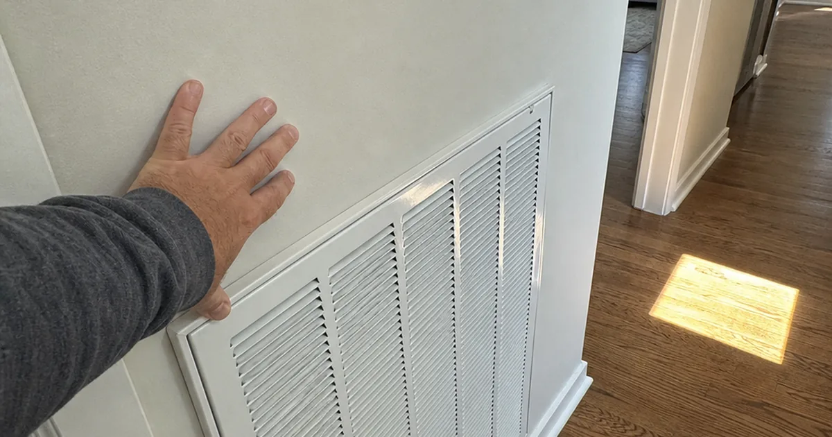 Home inspector's hand resting near an undersized HVAC return air grille in a sunlit Garden Grove hallway