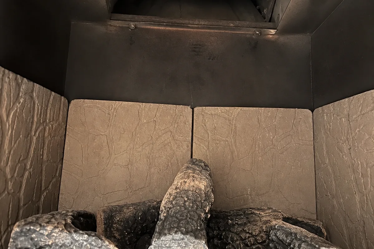 Ceramic gas-log burners inside a metal firebox with the throat damper open and no clamp holding it in place