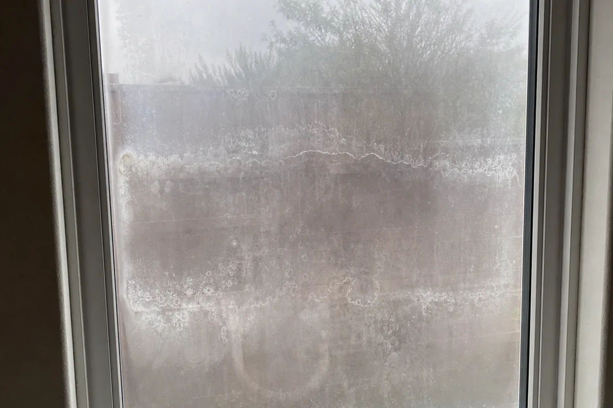 Failed dual-pane window with milky cloudy film and blotchy mineral haze trapped between the glass panes