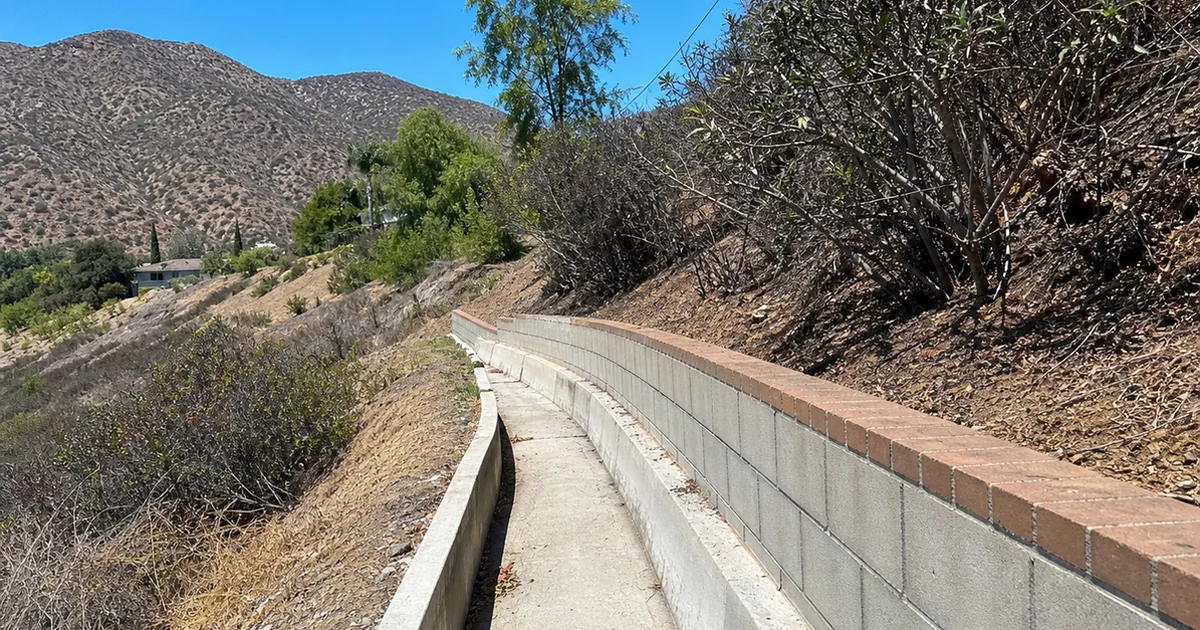 Concrete drainage channel and retaining wall along a chaparral hillside lot below dry foothills in La Cañada Flintridge