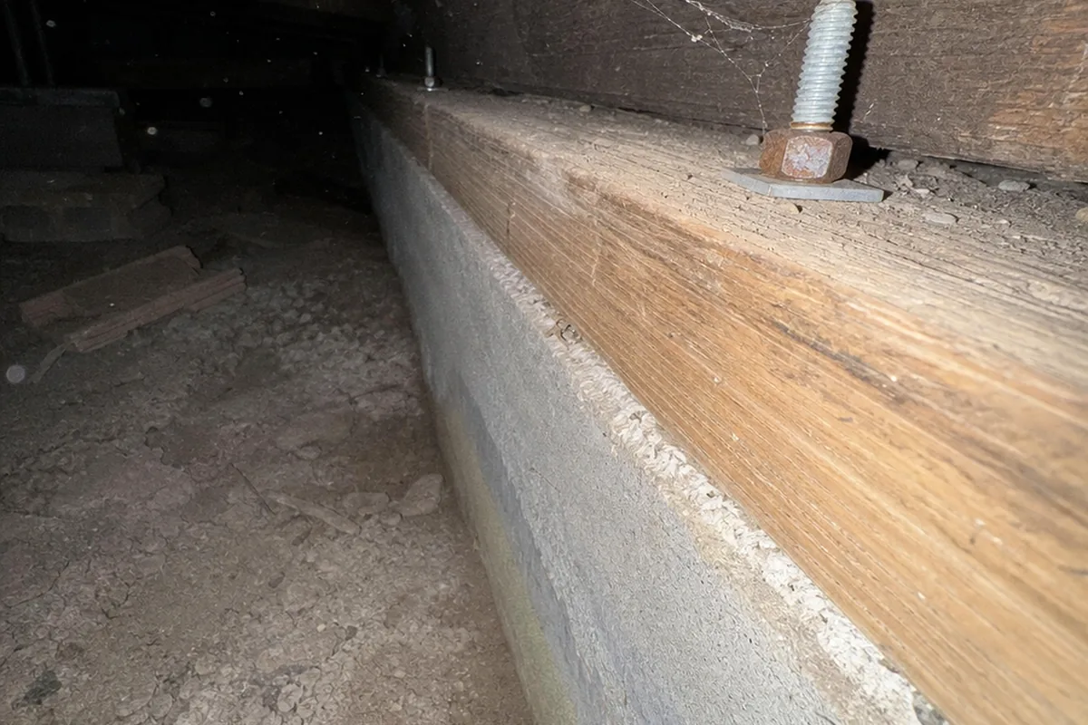 Galvanized anchor bolt with a square washer and hex nut through a crawlspace mudsill on a concrete stem wall