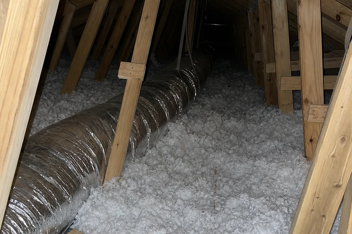 New attic bay with clean engineered roof trusses, fresh loose-fill insulation, and a flexible duct run