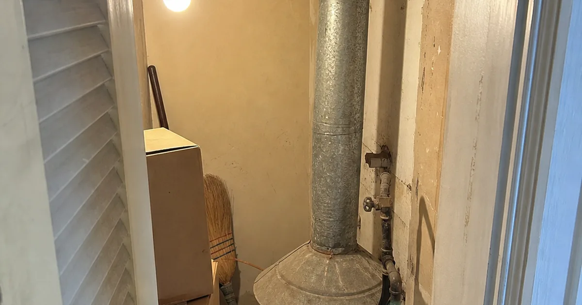 A gas water heater's draft hood and single-wall vent connector in a tight Norwalk utility closet, with a louvered door partly obstructed by stored boxes