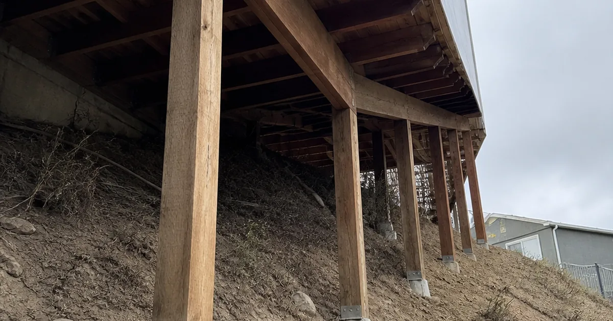 Tall wood posts stepping down a steep Oakland hillside carrying the floor framing of a house below its street-level garage