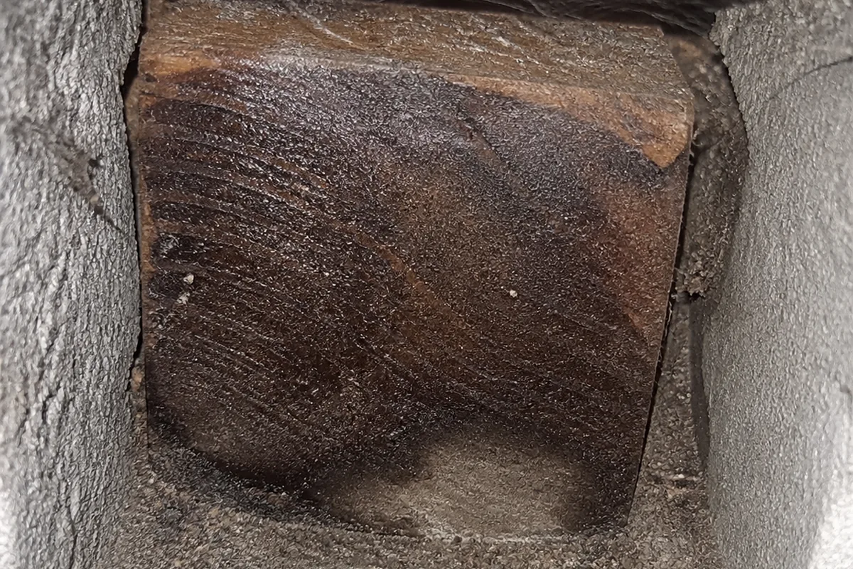 A wood girder end bearing tightly into a concrete foundation pocket with no air gap around it, dark moisture staining spreading into the end grain