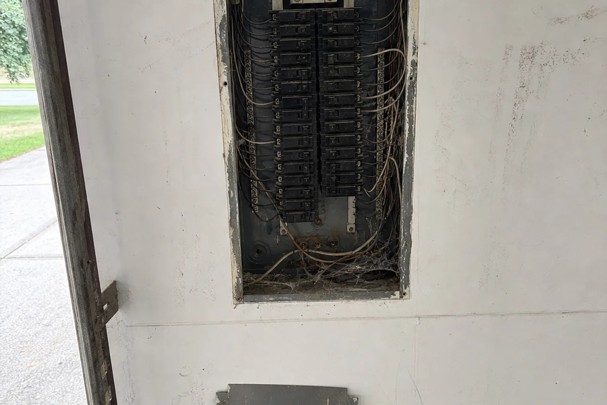 Open service panel with the deadfront removed, showing aged breakers and a bundle of branch wiring