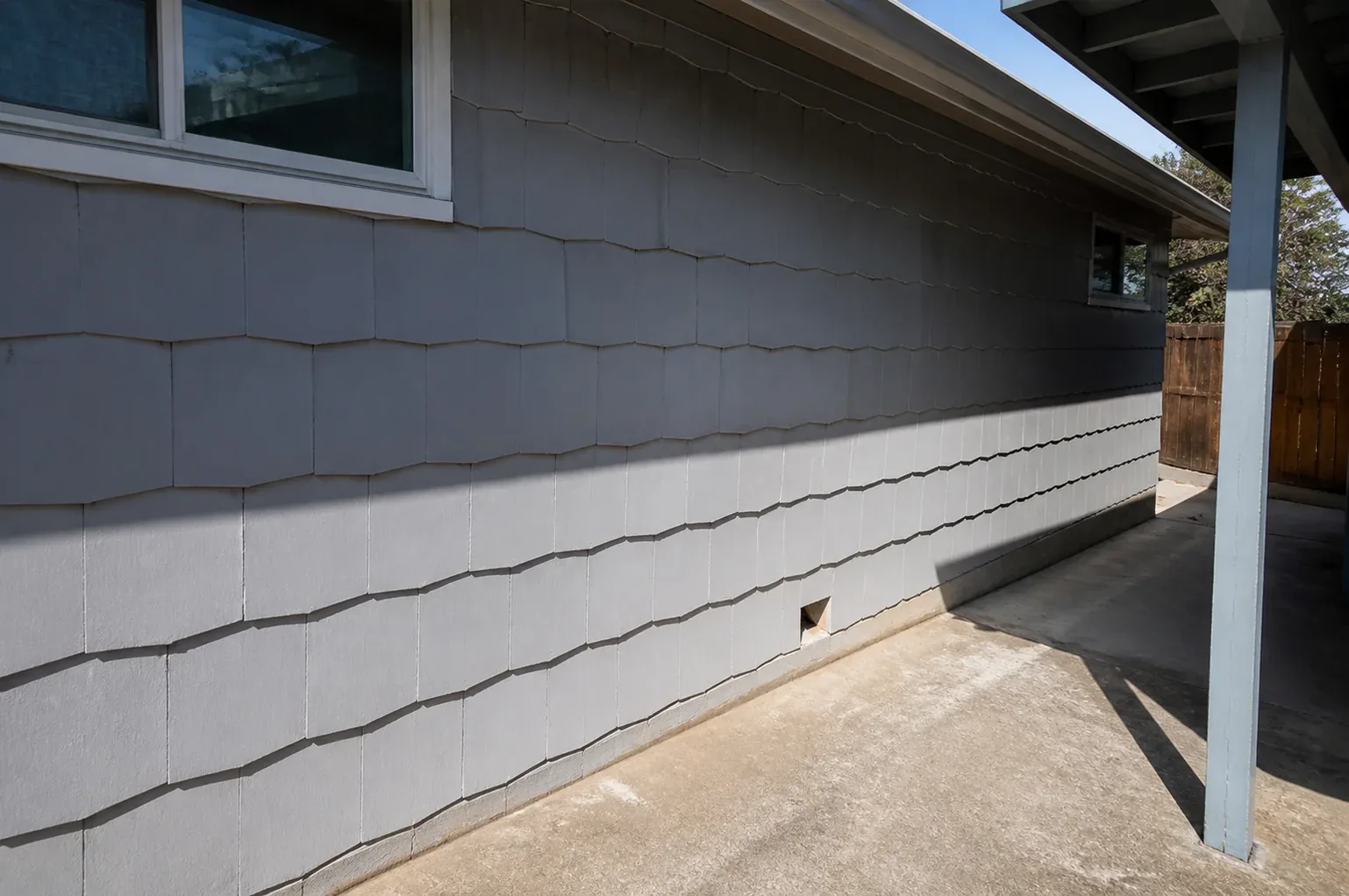 A row of gray asbestos cement siding shingles on the exterior wall of a Panorama City post-war tract home, showing the material's distinctive rigid panel pattern