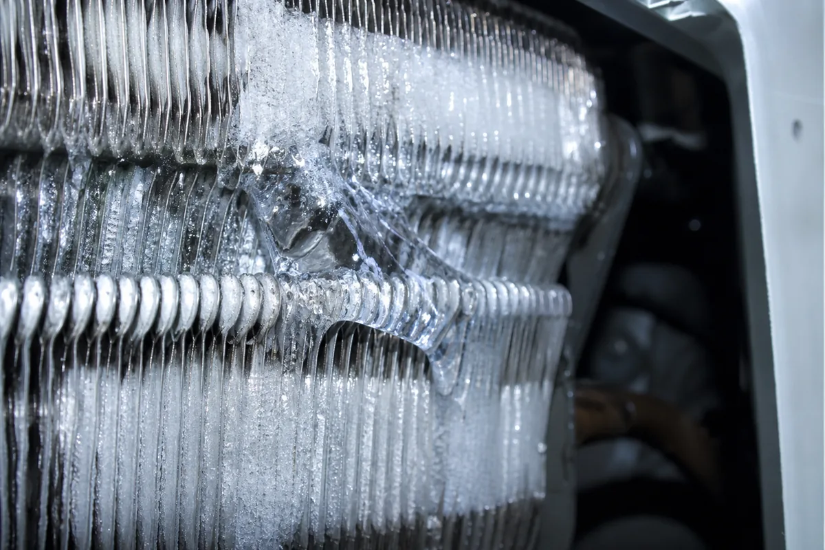 A close macro view of ice buildup on an air conditioning evaporator coil, evidence of restricted airflow or low refrigerant charge