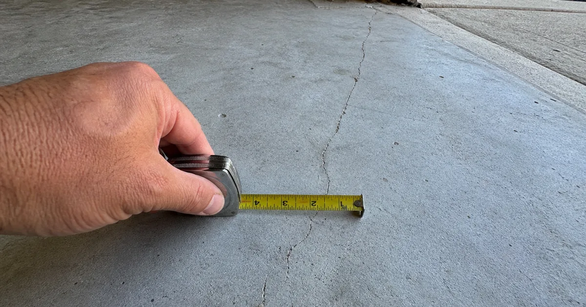 Home inspector measuring a hairline crack across a bare concrete garage slab with a tape measure in a Rancho Cucamonga home