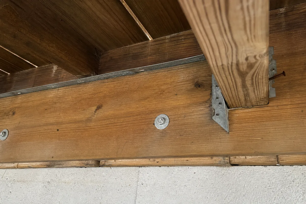 View from underneath a deck looking up at the ledger board and rim joist connection, showing whether metal flashing is present at the joint
