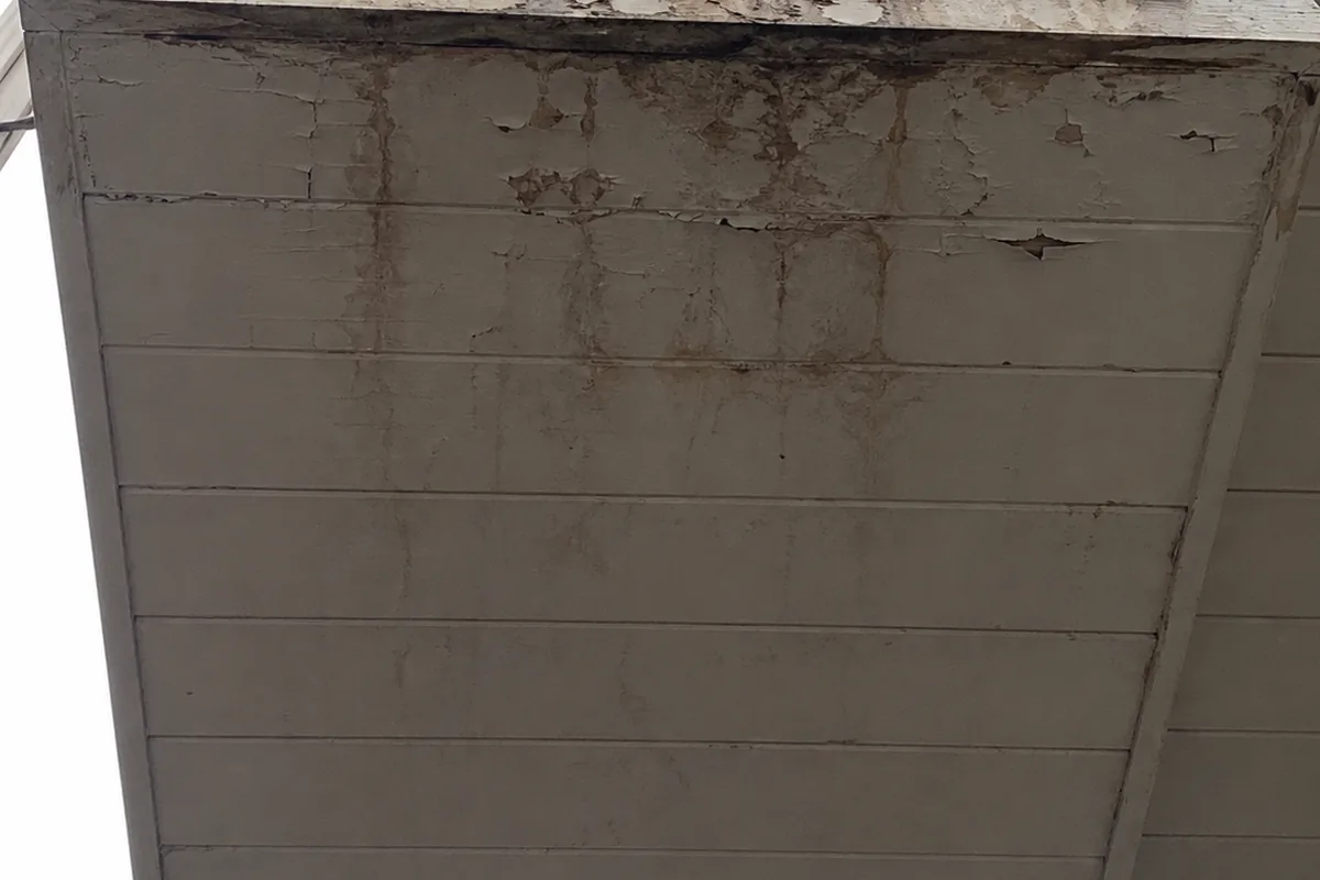 Looking straight up at the underside of a projecting bay window where the siding meets trim, with dark staining spreading along the joint