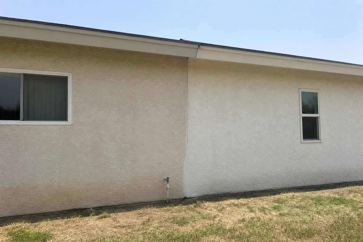 A crack running down the exterior stucco wall of a Santee single story home, tracking the vertical seam where an added room meets the original house, with the roof eave line stepping slightly at the same point