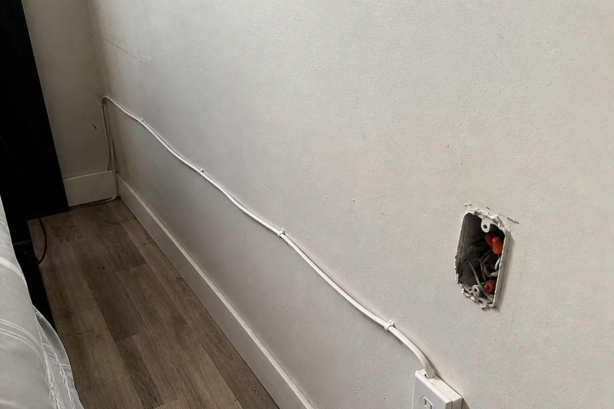 Amateur surface-run cable stapled along a converted garage wall to a surface-mounted outlet box, with an open junction box beside it