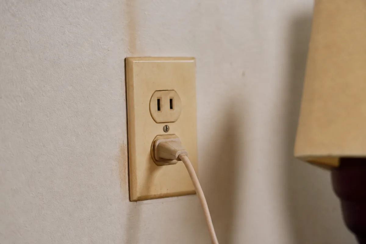 Older two-prong ungrounded outlet in a yellowed ivory cover plate on an aged plaster wall